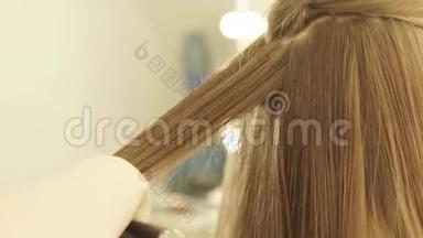 发型师梳长发，在美发沙龙用发钳矫直。 关闭女理发师