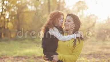 一位美丽的妈妈和她可爱的女儿正在秋天的公园里散步。 妈妈把女儿抱在怀里。 他们