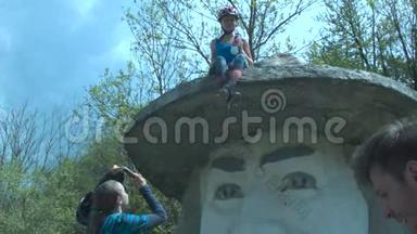 游客们被拍到戴着帽子的大头纪念碑。 一个戴着头盔的年轻女孩坐在纪念碑`帽子上。 A.