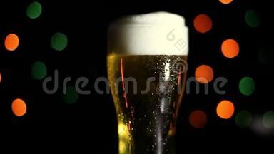 黑色背景上的一杯冷啤酒，有彩灯。 水滴顺着玻璃流下来。