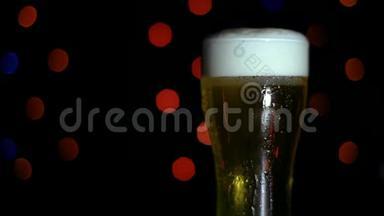 酒吧里有一杯黑色背景上的冷啤酒，上面有彩灯。 啤酒在玻璃杯里起泡。