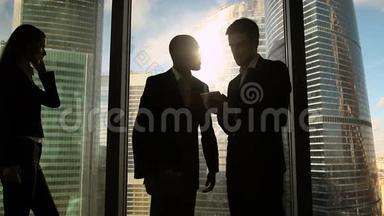 两个多<strong>文化</strong>的商人站在<strong>办公室</strong>的窗口边说话握手