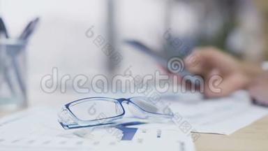 桌子上躺着眼镜，智能手机上的女人滚动页面，办公室休息