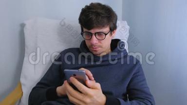 戴眼镜的男人坐在扶手椅上用智能<strong>手机浏览</strong>社交媒体。