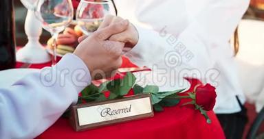 情侣牵手的浪漫户外晚餐.. 桌子上装饰着保留的牌匾和红玫瑰。 没有脸。 4k