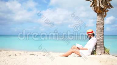 年轻女子<strong>坐在</strong>棕榈<strong>树下</strong>的白色海滩上看书