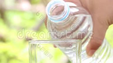 女人手拿水瓶，在模糊的绿色自然背景上向玻璃中倒入清澈的饮用水。