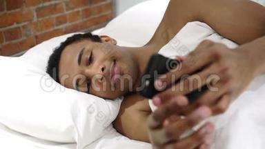 在床上使用智能手机浏览互联网的非洲男子