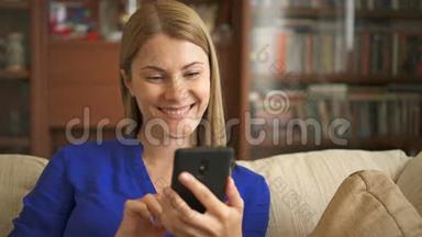 女人拿着智能手机坐在沙发上。 浏览互联网微笑，与她的朋友交流