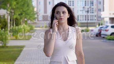 一位手里拿着手机的年轻女子在<strong>夏日</strong>的<strong>大</strong>街上自信地走着，一位女士正在谈论一个