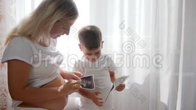 年轻的怀<strong>孕妈妈</strong>，带着甜美的孩子，在明亮的自然光线下在家里看摄影声像
