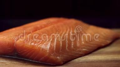 将新鲜美味的三文鱼牛排放在木切割板上，隔离在黑色背景上。 生的红鱼片