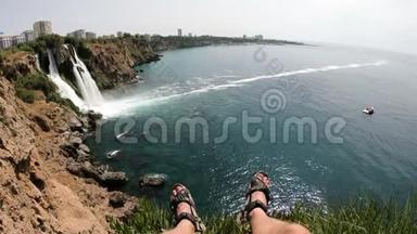 坐在悬崖上的人的腿和欣赏安塔利亚瀑布的图片