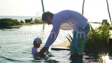 父亲带着一个孩子在海滩旁边的游<strong>泳池里玩耍</strong>，日落时分。 热带岛屿