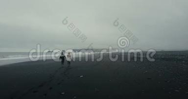 这对年轻夫妇穿着冰岛毛衣，在冰岛黑色火山海滩的海边漫步