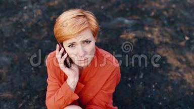 非常<strong>悲伤</strong>的红发女人坐在烧焦的草地上，拿着电话对着耳朵。 概念：需要帮助，<strong>悲伤</strong>，孤独