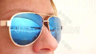 一个戴太阳镜的快乐女人的特写脸。 与休息的人的海滩反映在眼镜上。 4k，慢