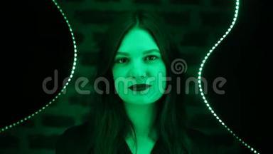 年轻漂亮的女孩在绿色霓虹灯上突出了镜子的背景。 夜店霓虹灯时尚风格黑色红唇