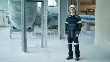 年轻工程师戴着防护头盔，在现代化工厂里摆着相机