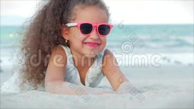 <strong>粉色</strong>眼镜中美丽的小女孩的特写镜头，可爱的<strong>微</strong>笑看着镜头，躺在沙滩上