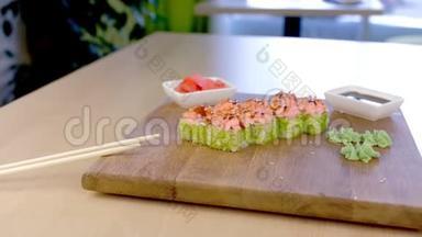 加了绿色鱼子酱和酱汁的卷在木板上，芥末、生姜和酱油在咖啡馆的桌子上。