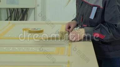 在一家工厂，一名妇女用一条保护胶带把室内木门的生产贴在门上