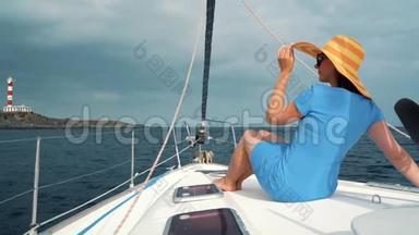穿着黄色帽子和<strong>蓝色</strong>礼服的女人在海洋的<strong>夏季</strong>靠近灯塔的游艇<strong>上</strong>休息。 慢动作