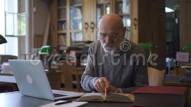 成熟的教授用书和笔记本电脑工作，坐在图书馆的桌子旁。