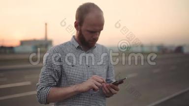 一个年轻人在日落或日出时在街上使用他的智能手机