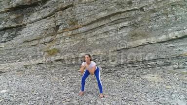 女人在岩石背景上做呼吸练习时蹲着身体反射。 空中美丽的画面。