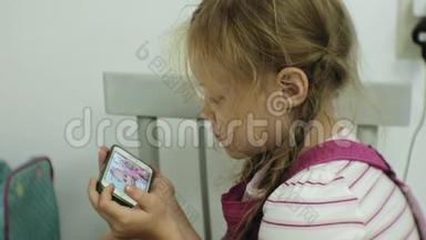 坐在椅子上的小女孩试图用她的智能<strong>手机玩</strong>游戏。 儿童使用<strong>手机</strong>