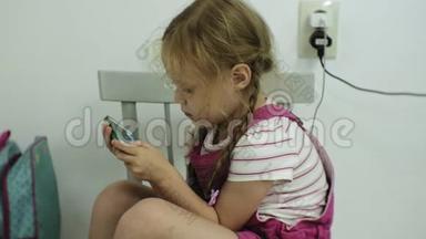 坐在椅子上的小女孩试图用她的智能手机玩游戏。 儿童使用手机