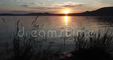 美丽的夏天日落在一个山湖上。 红日落山.. 波浪向岸上奔流