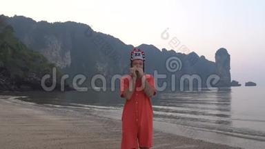 在泰国海岸线上的黄昏时分，戴着传统泰国女帽的古怪的白种人用竖琴演奏