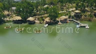 木制平房与茅草屋顶和船码头在海岸绿湖度假酒店无人驾驶飞机视图。 岸上的小屋