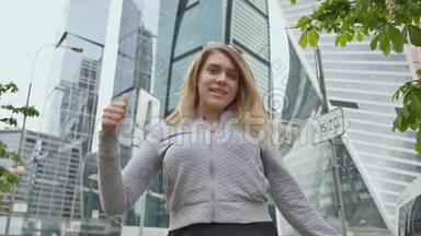 年轻快乐的金发女孩，在高楼大厦和摩天大楼的背景下竖起大拇指