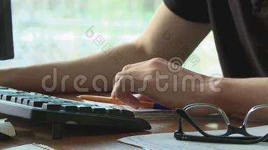 男人的双手放在<strong>键盘</strong>上，在电脑旁工作，桌子旁边放着眼镜，有记录的<strong>文件</strong>