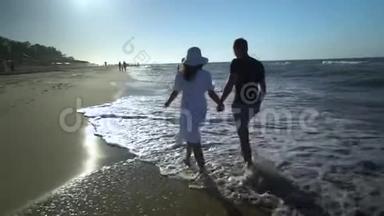 一对年轻夫妇正沿着海滨散步。 他们相爱，牵手。 晴朗，阳光明媚的一天.. 一个女孩