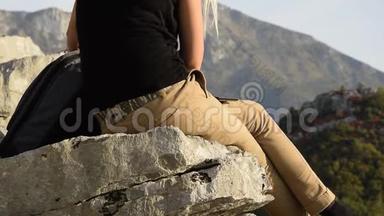 年轻女子在坐在山崖边上的美丽山峰上寻找背包里的东西