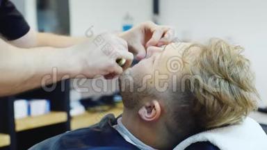 一个年轻人在理发店用危险的剃<strong>刀刮胡子</strong>