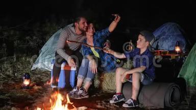 爸爸妈妈带着儿子在篝火旁的大自然中的android上拍照，幸福的家庭在手机上拍照