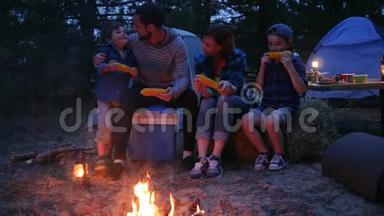 在大自然的火焰附近吃晚餐，家人用盐吃玉米，旅行野营，妈妈，爸爸和儿子吃新鲜的黄色玉米