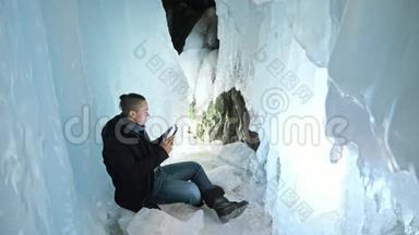 人类坐在冰<strong>洞</strong>里的平板电<strong>脑</strong>上。 围绕着神秘美丽的冰窟.. 用户在