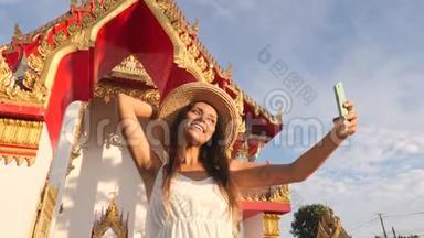 穿着白衣服、戴着大草帽的年轻旅游女孩在<strong>泰国佛寺</strong>用手机拍照