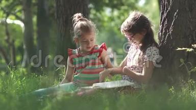 孩子们坐在树旁的<strong>草地上</strong>看一本书。 两个<strong>小女孩</strong>一起玩