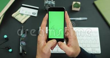 男人拿着一个绿色屏幕的黑色智能手机，在工作桌上<strong>敲</strong>了<strong>敲</strong>它的东西