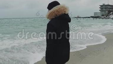 在寒冷的冬天，年轻漂亮的女人在海滩上走来走去。 慢动作