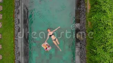 一位年轻的女游客在私人游泳池的一张漂浮的桌子上享用自己的私人早餐