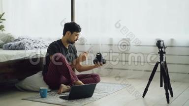 帅哥摄影师录制视频博客，介绍家里坐在床边的摄影设备