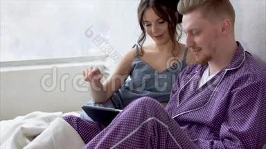 两个穿着睡衣，坐在床上看着平板电脑上的新赛季。